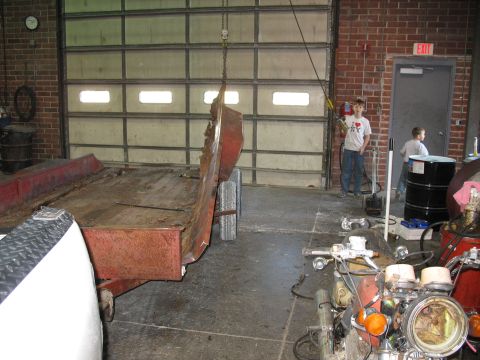 1900 Ford C-350 (Centurion Conversions) - Trailer and motorcycle parts in a garage setting with children present.