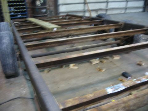 1900 Ford C-350 (Centurion Conversions) - The rusty frame of a trailer sits in a workshop, with tires visible on the left side.