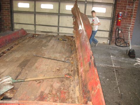 1900 Ford C-350 (Centurion Conversions) - A person observes as a section of a damaged trailer bed is removed, revealing worn wooden planks and debris.