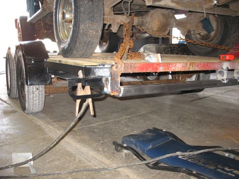 1900 Ford C-350 (Centurion Conversions) - A trailer is loaded with vehicle components, including axles and wheels, secured by heavy chains.