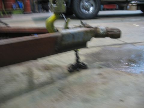 1900 Ford C-350 (Centurion Conversions) - A crane is lifting a trailer hitch assembly in a workshop. A truck is parked in the background.
