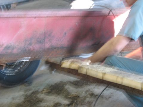 1900 Ford C-350 (Centurion Conversions) - A person is seen working on the frame of a red trailer, using wood blocks for support.