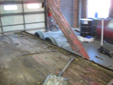 1900 Ford C-350 (Centurion Conversions) - A trailer bed with two tires and a red metal beam is shown in a garage setting.