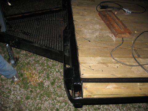 1900 Ford C-350 (Centurion Conversions) - A close-up view of a trailer's wooden deck and ramp, showing some electrical components and a rusty metal bar.
