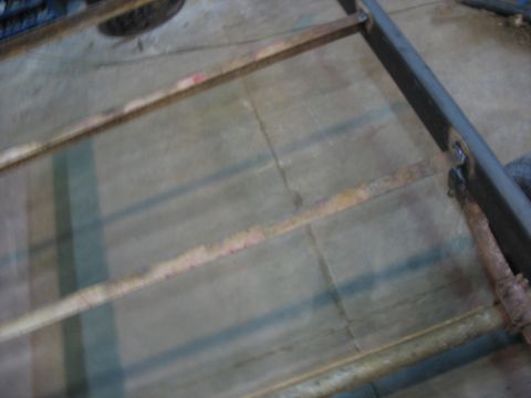 1900 Ford C-350 (Centurion Conversions) - A close-up view of a metal frame structure, showing signs of wear and tear on a concrete surface.