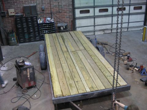 1900 Ford C-350 (Centurion Conversions) - A newly constructed wooden deck sits atop a flatbed trailer inside a garage or workshop.