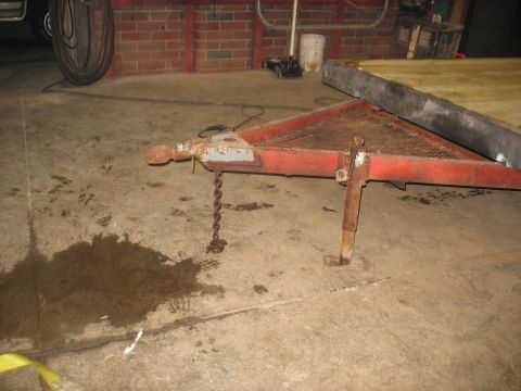 1900 Ford C-350 (Centurion Conversions) - Trailer hitch and jack stand on a concrete floor with a puddle of liquid.