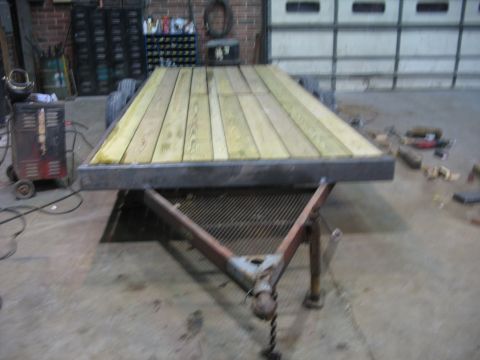1900 Ford C-350 (Centurion Conversions) - A trailer with a newly installed wooden deck sits in a workshop, with tools and equipment visible in the background.