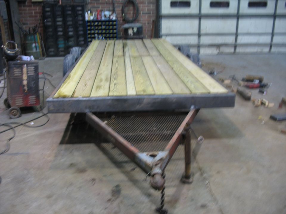 Flatbed trailer with a new wooden deck in a garage. A welding machine is to the left