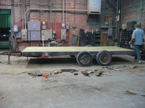 1900 Ford C-350 (Centurion Conversions) - A flatbed trailer sits in a workshop, surrounded by tools and building materials.
