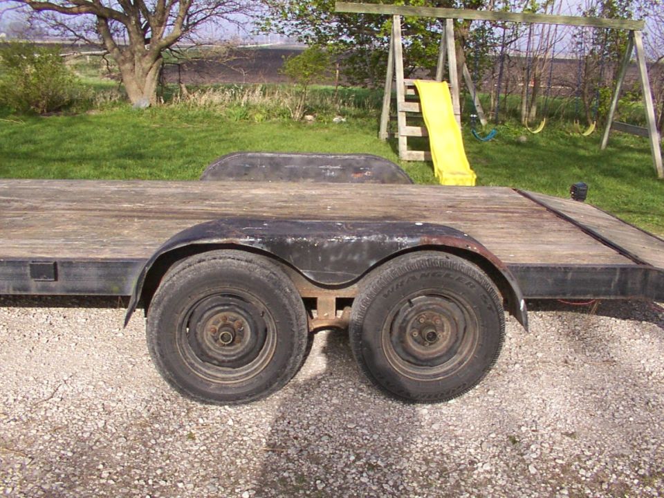Dual axle trailer with wooden deck and metal fenders. Backyard with a swing set and slide in the background