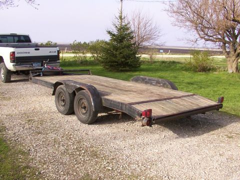 1900 Ford C-350 (Centurion Conversions) - A white Dodge pickup truck is hitched to a wooden car hauler trailer on a gravel driveway.