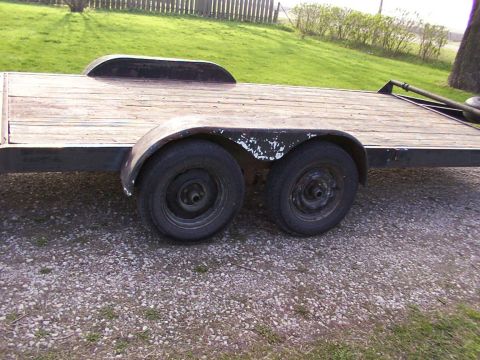 1900 Ford C-350 (Centurion Conversions) - A side view of a trailer with two axles and a wooden deck, parked on gravel.