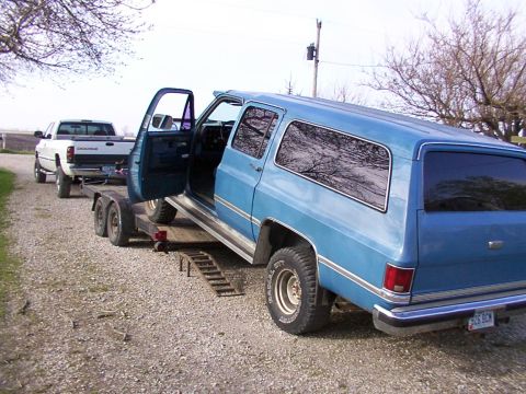 1900 Ford C-350 (Centurion Conversions) - Blue SUV loaded onto a trailer, with a white Dodge pickup truck visible behind it.