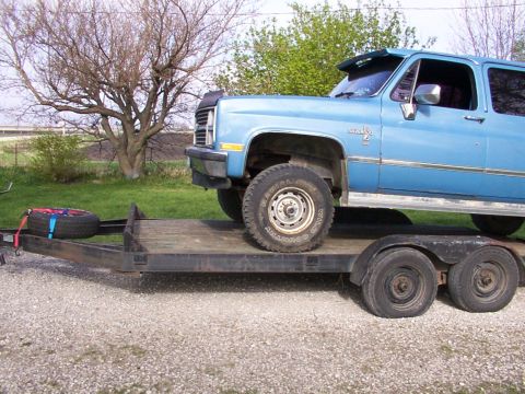 1900 Ford C-350 (Centurion Conversions) - A blue SUV is loaded onto a flatbed trailer, with a spare tire secured to the front of the trailer.