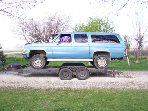 1900 Ford C-350 (Centurion Conversions) - Blue Chevrolet Suburban loaded onto a trailer, viewed from the side. The vehicle appears to be from the 1980s.