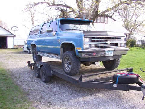 1900 Ford C-350 (Centurion Conversions) - A blue SUV is transported on a trailer, showing its front three-quarter view and a license plate reading S26 BCM.