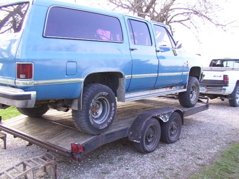 1900 Ford C-350 (Centurion Conversions) - Blue SUV being transported on a trailer, with a white pickup truck in the background.