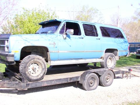 1900 Ford C-350 (Centurion Conversions) - An extended blue SUV is loaded onto a trailer, showing its lifted suspension and large off-road tires.