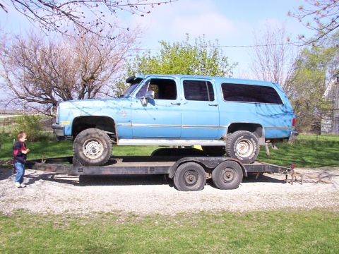 1900 Ford C-350 (Centurion Conversions) - Blue Chevrolet Suburban loaded onto a trailer, with a young child observing.