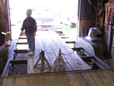 1900 Ford C-350 (Centurion Conversions) - A young boy stands on a wooden trailer inside a garage, holding a tool.