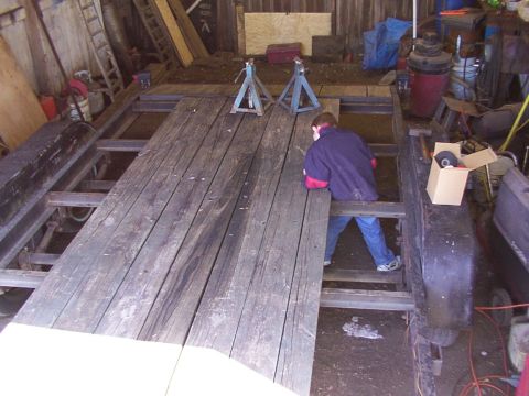 1900 Ford C-350 (Centurion Conversions) - A person works on a trailer frame with wooden planks inside a barn.