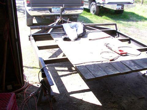 1900 Ford C-350 (Centurion Conversions) - A trailer is parked in front of two trucks, with a saw and a blue tarp on its surface.