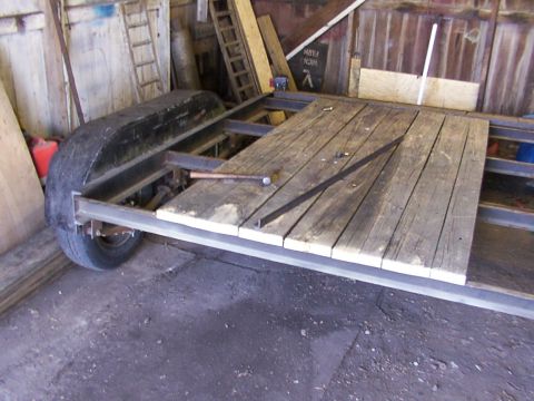 1900 Ford C-350 (Centurion Conversions) - A partially constructed trailer with a wooden deck sits inside a workshop.