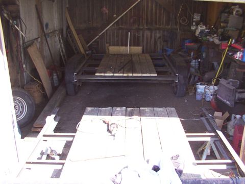 1900 Ford C-350 (Centurion Conversions) - A trailer frame with wooden deck sections is visible in a workshop setting, surrounded by tools and materials.
