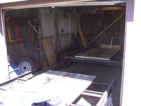 1900 Ford C-350 (Centurion Conversions) - Two trailers, one with wooden decking, sit in a garage filled with tools and supplies.