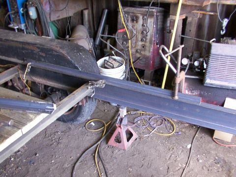 1900 Ford C-350 (Centurion Conversions) - Metal beams are being welded together to form a trailer frame in a cluttered workshop.