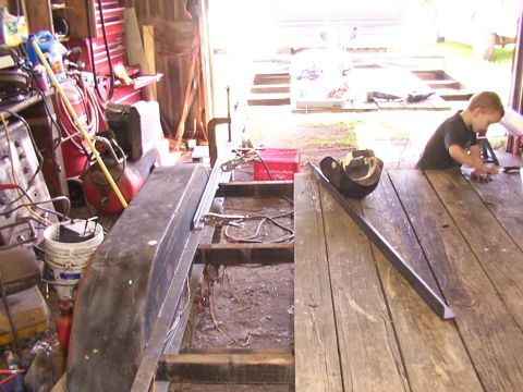 1900 Ford C-350 (Centurion Conversions) - A young boy works on a table next to a trailer frame in a cluttered garage.