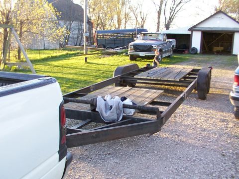 1900 Ford C-350 (Centurion Conversions) - A gray pickup truck is parked next to a tandem axle trailer in a gravel driveway, with a horse trailer visible in the background.