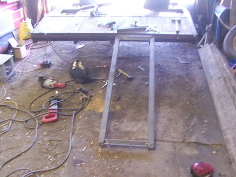 1900 Ford C-350 (Centurion Conversions) - A metal trailer frame sits on the floor of a workshop, surrounded by tools and building materials.