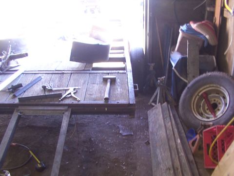 1900 Ford C-350 (Centurion Conversions) - Tools and materials are laid out on a wooden trailer frame inside a cluttered garage.