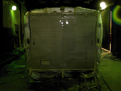 1900 Ford C-350 (Centurion Conversions) - The rear of a large, enclosed vehicle is covered in plastic sheeting, suggesting it is being prepared for transport or storage.