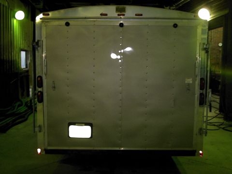 1900 Ford C-350 (Centurion Conversions) - The rear of a silver enclosed trailer is shown, illuminated by overhead lights.