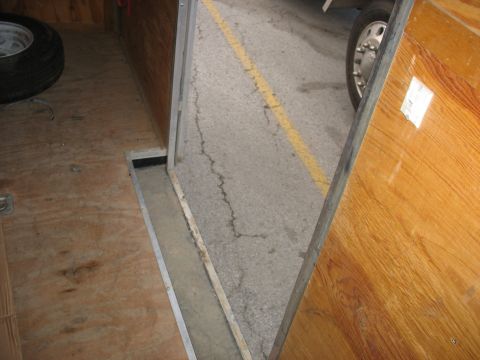 1900 Ford C-350 (Centurion Conversions) - View from inside a trailer looking out at a paved area with a yellow line and a vehicle's wheel.