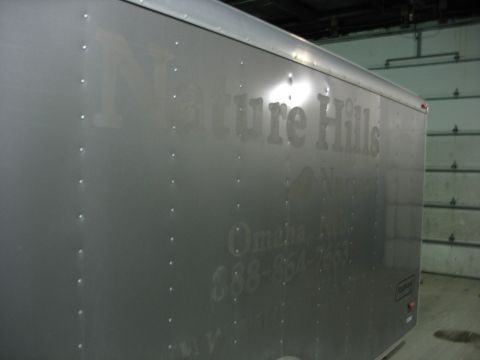 1900 Ford C-350 (Centurion Conversions) - A silver enclosed trailer with 'Nature Hills Nursery' and a phone number is parked in front of a garage door.