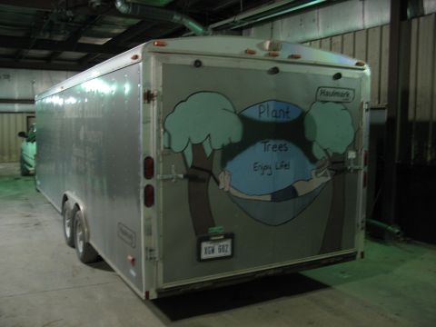 1900 Ford C-350 (Centurion Conversions) - The back of a silver enclosed trailer features a colorful mural with trees and a hammock, along with a license plate.