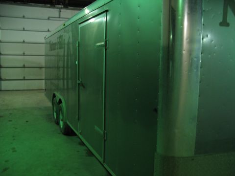 1900 Ford C-350 (Centurion Conversions) - A green cargo trailer is parked inside a garage with white roll-up doors in the background.