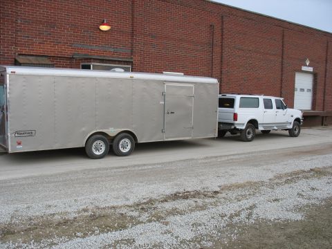 1900 Ford C-350 (Centurion Conversions) - White Ford SUV towing a silver cargo trailer in front of a brick building.