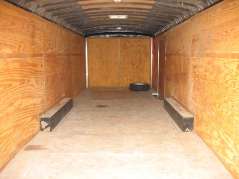 1900 Ford C-350 (Centurion Conversions) - The interior of a cargo trailer, showing its wooden walls and floor, with a spare tire visible.
