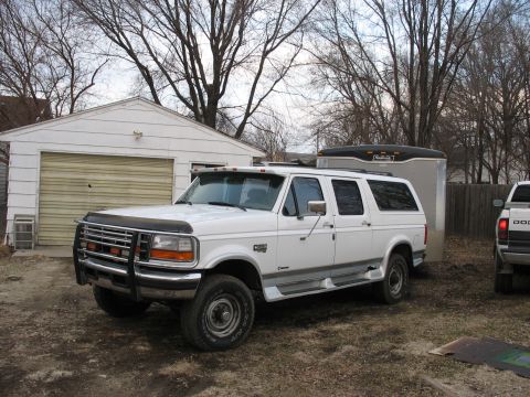 1900 Ford C-350 (Centurion Conversions) - A white Ford SUV is parked in front of a garage with a trailer attached.