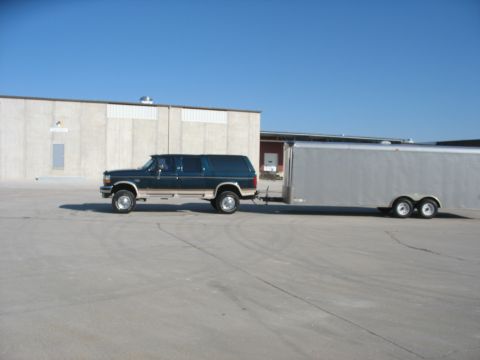1900 Ford C-350 (Centurion Conversions) - Dark green Ford SUV towing a silver enclosed trailer on a paved lot.