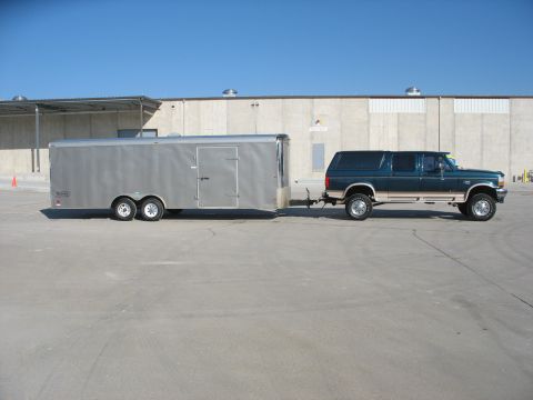 1900 Ford C-350 (Centurion Conversions) - A Ford Bronco SUV is parked outside a commercial building, attached to a large silver trailer.