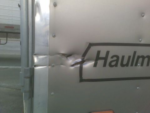 1900 Ford C-350 (Centurion Conversions) - Close-up of a dented trailer side the "Haulmark" logo, indicating damage to the vehicle's exterior.