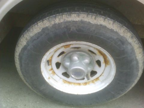 1900 Ford C-350 (Centurion Conversions) - Close-up of a trailer's wheel and tire, showing signs of wear and rust on the rim.