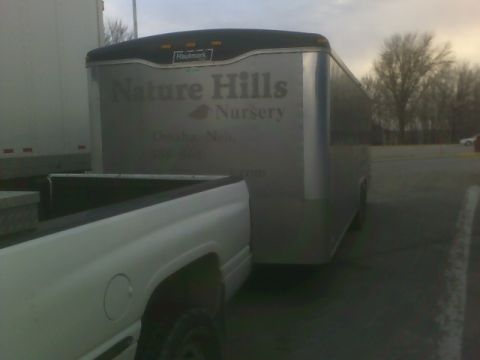 1900 Ford C-350 (Centurion Conversions) - A trailer with "Nature Hills Nursery" branding is parked next to a white pickup truck.