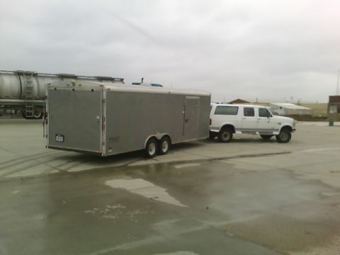 1900 Ford C-350 (Centurion Conversions) - A white Ford Bronco SUV is parked next to a large silver enclosed trailer on a cloudy day.